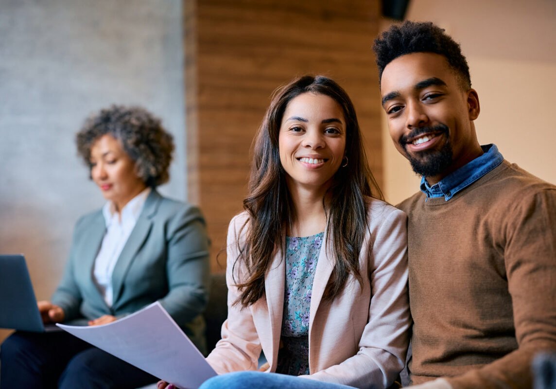 Happy African American couple having a meeting with their insurance agent in the office and looking at camera.